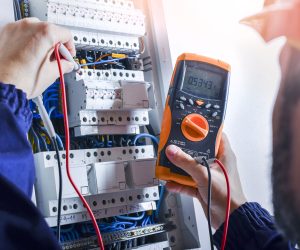 Electrician installing electric cable wires of fuse switch box. Multimeter in hands of electricians detail.